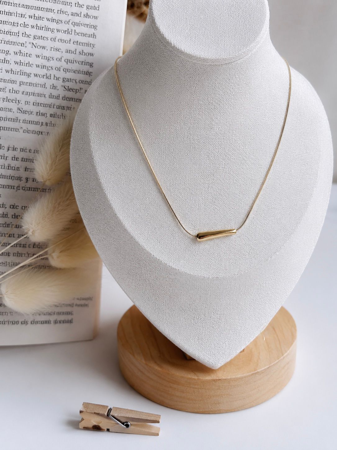 Gold necklace on a white bust with a wooden base, placed on a light surface.