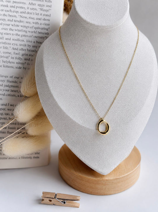 Gold necklace on a white bust with a book in the background