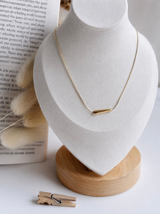 Gold necklace on a white bust with a wooden base, placed on a light surface.