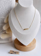 Gold necklace on a white bust with a wooden base, placed on a light surface.