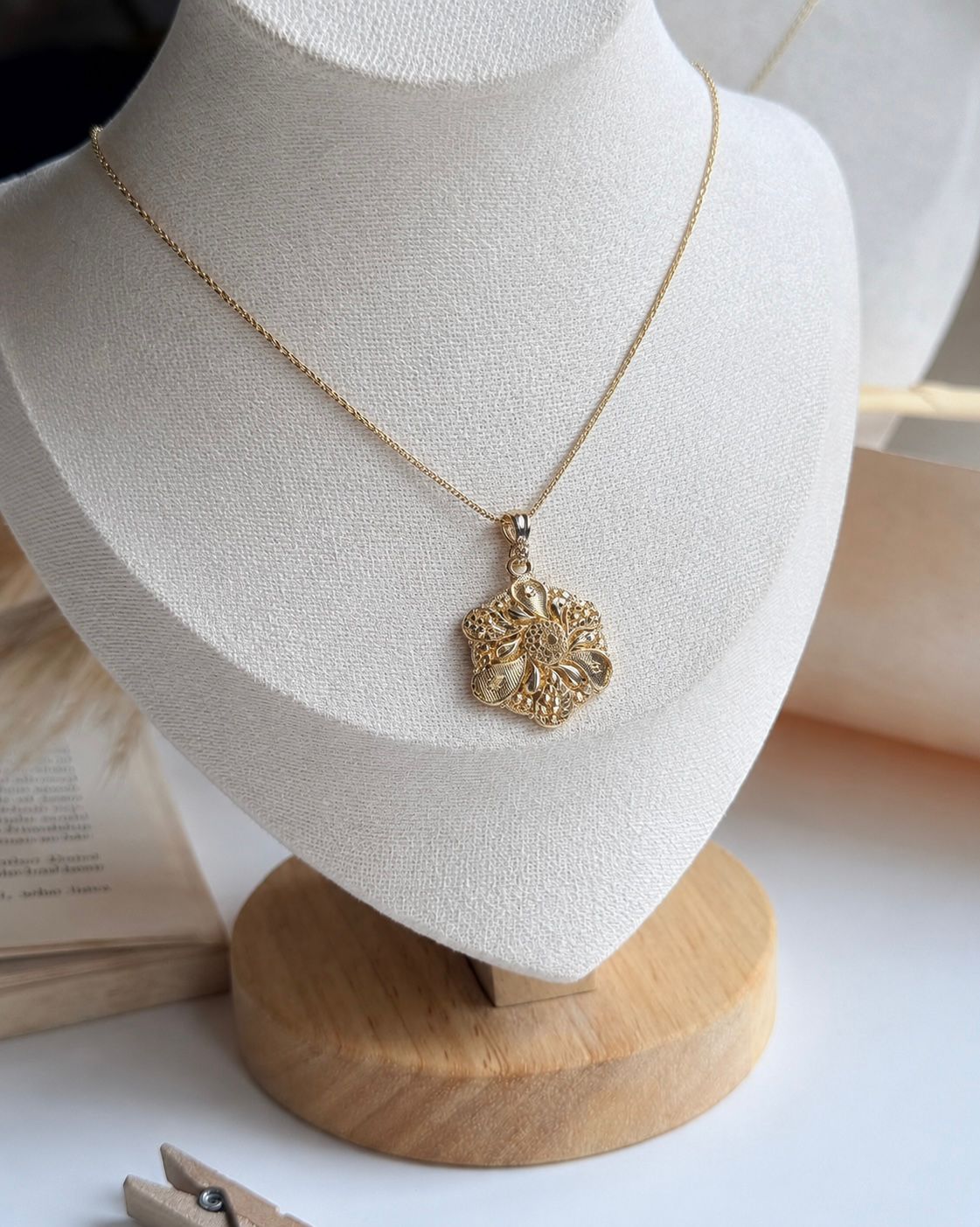 Gold necklace with a detailed pendant on a white mannequin bust.