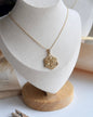 Gold necklace with a detailed pendant on a white mannequin bust.