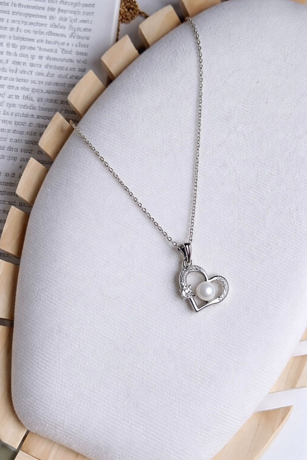 Heart-shaped necklace with a pearl pendant on a textured surface