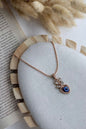 Necklace with an eye-shaped pendant on a textured surface next to dried plants.