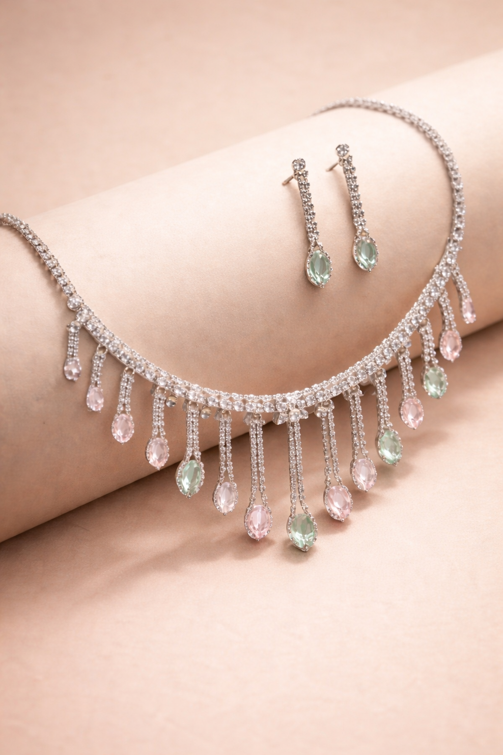 Necklace and earrings with teardrop-shaped gemstones on a soft pink background