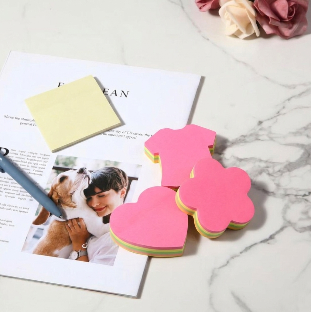 Flower-shaped pink sticky notes on a marble surface with a magazine and pen.